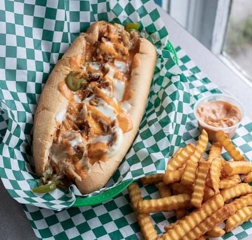 vegan cheesesteak covered in cheese and buffalo sitting in a green and white checkered paper next to french fries from trilly cheesesteaks in new orleans