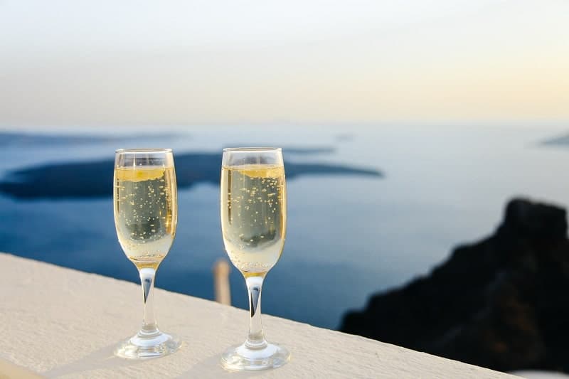 two sparkling wine glasses sitting on a railing that overlooks the blue sea