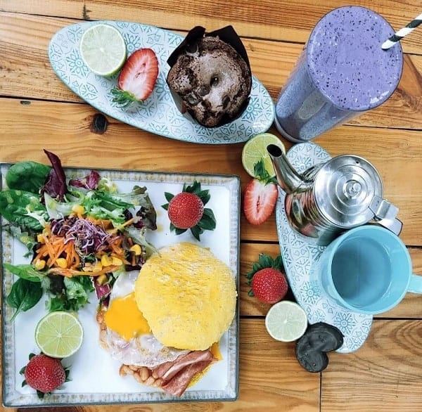 an overhead shot of a vegan brunch plate with fruit and salad, a purple smoothie and a muffin wrapped in a paper liner from veganitessan in seville