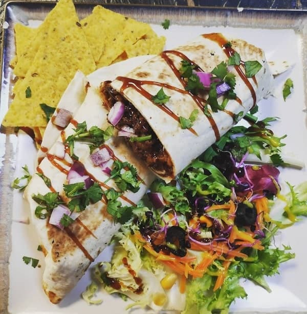 a large vegan burrito cut in half and covered with a dark sauce sitting on top of a bed of lettuce at veganitessan in seville