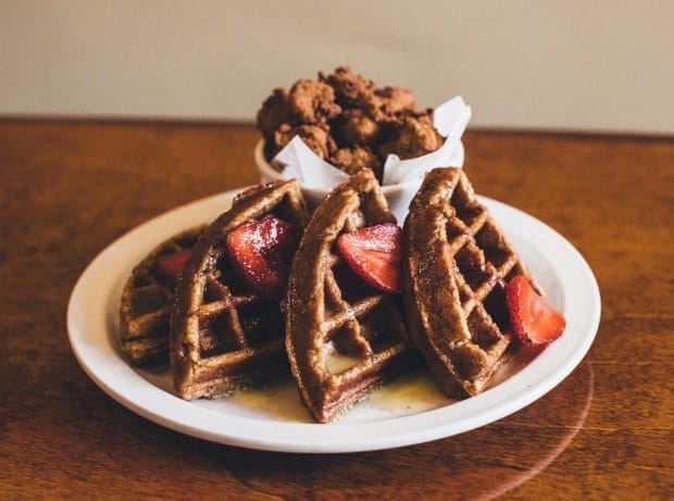 vegan waffles lined up with strawberries on a white plate in front of fried vegan chicken in detroit