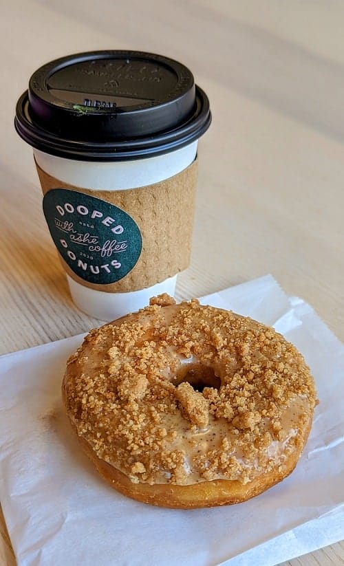 one large round vegan donut topped with sugar streusel in front of a to go cup of coffee in detroit