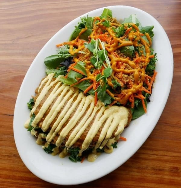 raw vegan burrito topped with cashew cream next to a green salad with carrots at judahlicious in san Francisco 