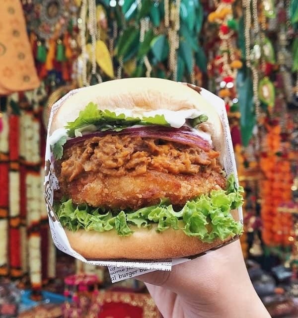 giant vegan chicken burger held in front of a colorful tapestry from veganburg in san Francisco
