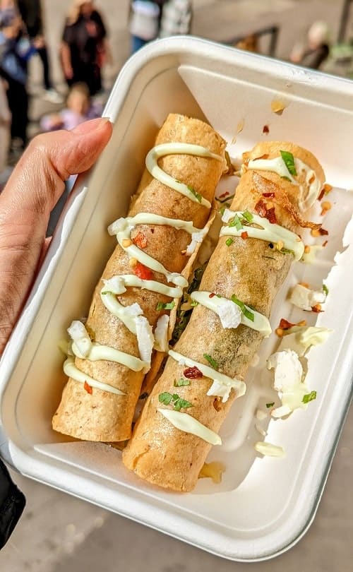 two golden crispy taquitos covered with an avocado cream sauce from antojitos in london