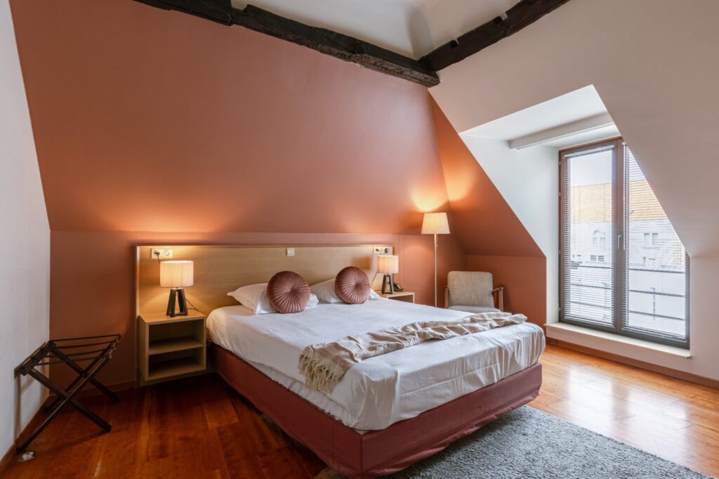 bright and modern guestroom with a double bed and a pink wall at the vegan hotel malleberg in bruges, belgium