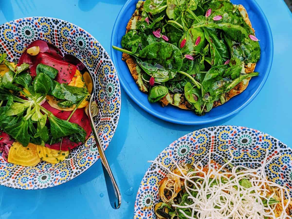 three colorful veggie dishes in intricately designed bowls on a blue table at DAR Vegan Restaurant Zurich