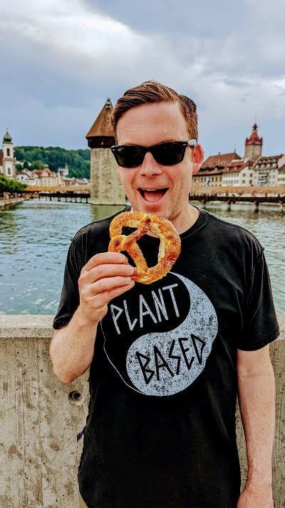 Matt Sawicki eating a Vegan Pretzel from Brezelkonig with the chapel bridge behind him