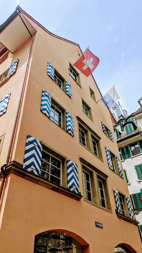 pink building with blue and white shutters in lucerne's old town with swiss and lucerne flags