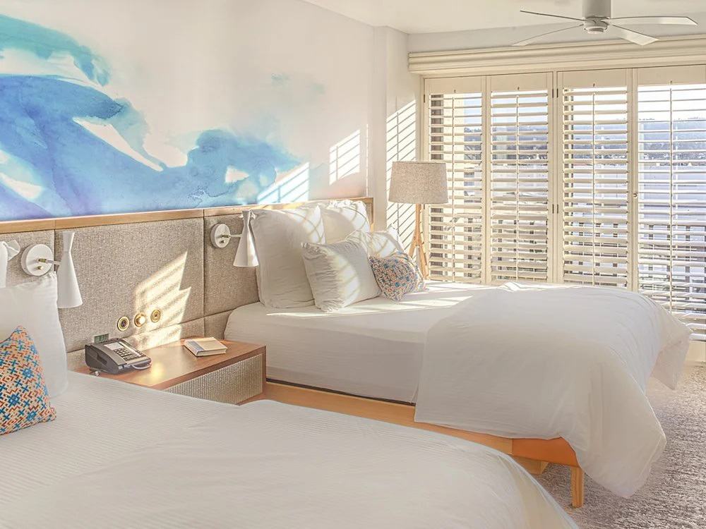 a modern guestroom with neutral colors and large windows with shutters at Portola Hotel & Spa at Monterey Bay