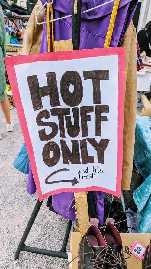 flea market sign created with a black sharpie that reads hot stuff only and his trash in front of a clothing rack