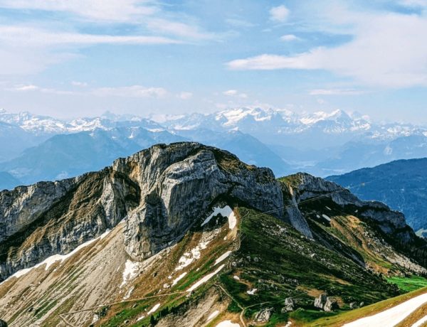 partly cloudy view from mount pilatus that shows green and snow covered mountain and the alps in the background