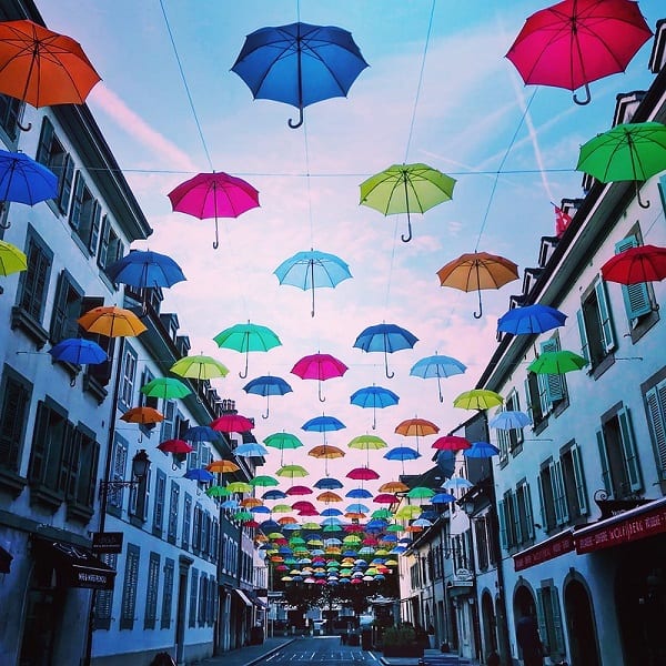 colorful umbrellas hung from above a narrow street on a cloudy day in carouge geneva