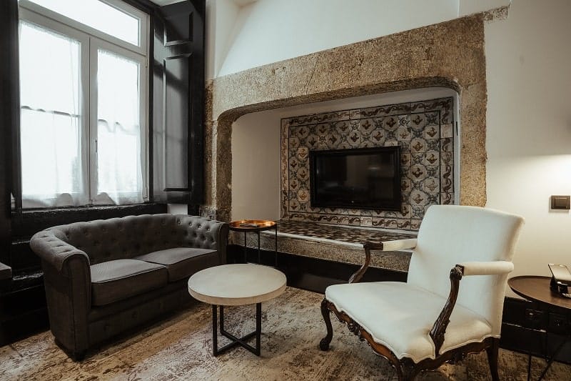 beautiful rustic guest room with a wood burning fire place, a white chair next to it and a dark couch with natural wood floors in lisbon at almalusa