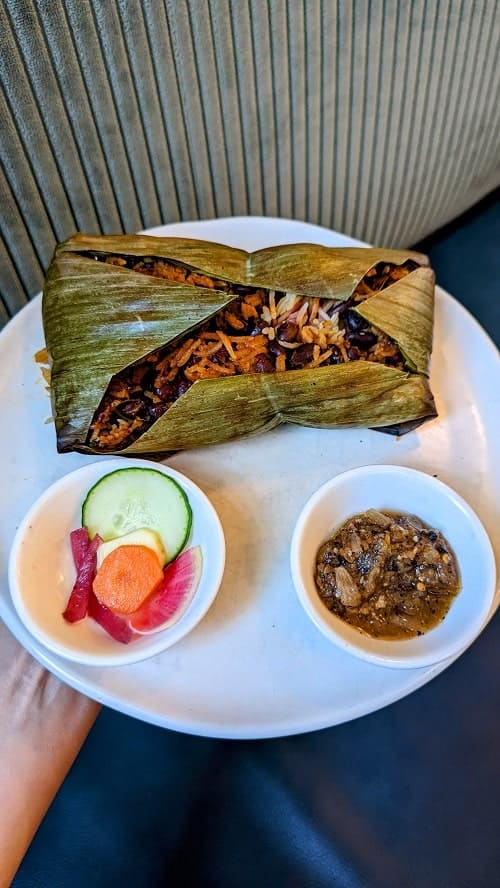 cut open banana leaf barbacoa with little bowls of sauce and pickled veggies on a white plate from rosalinda in toronto