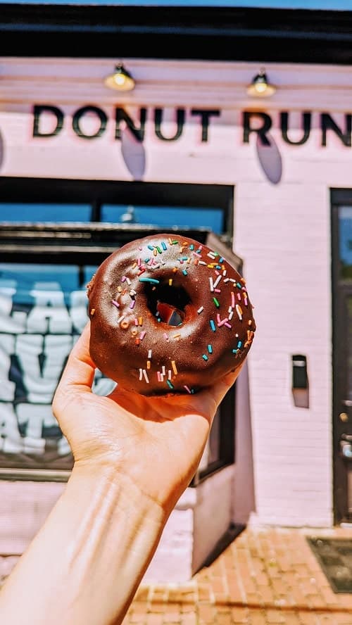 vegan chocolate sprinkle donut in front of the pink donut run store washington dc
