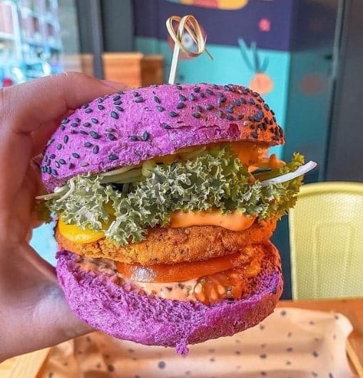 vegan burger with a bright purple hamburger bun, leafy greens, and colorful sauces in rome
