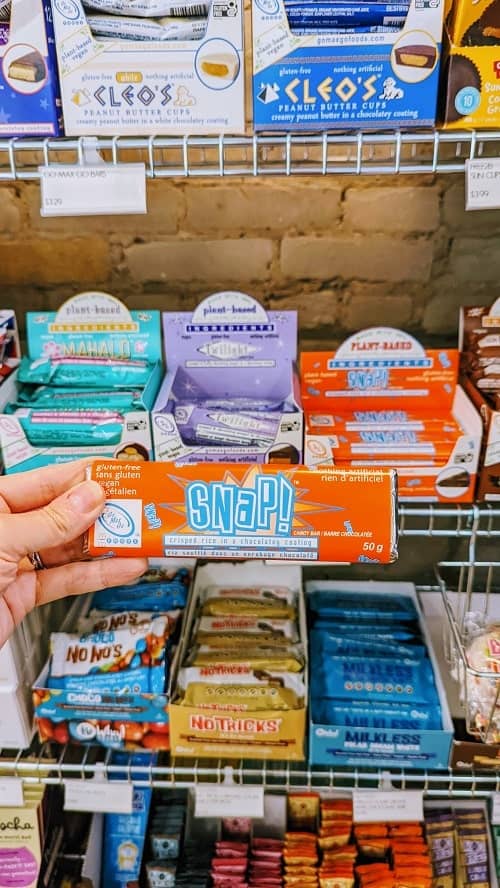 snap vegan chocolate bar in orange packaging held in front of a display of vegan chocolates at good rebel vegan provisions 