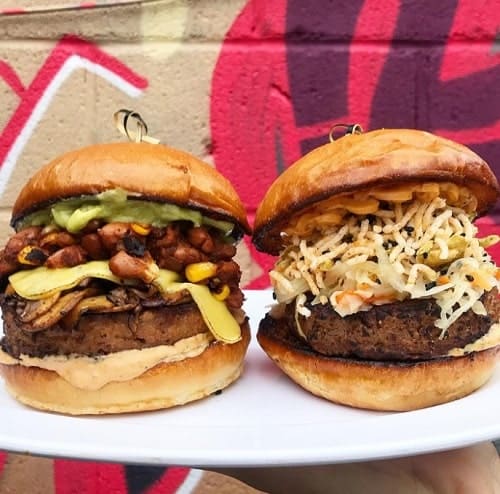 two giant vegan burgers next to each other stuffed with cheese, slaw, and avocado at guerilla burger in toronto
