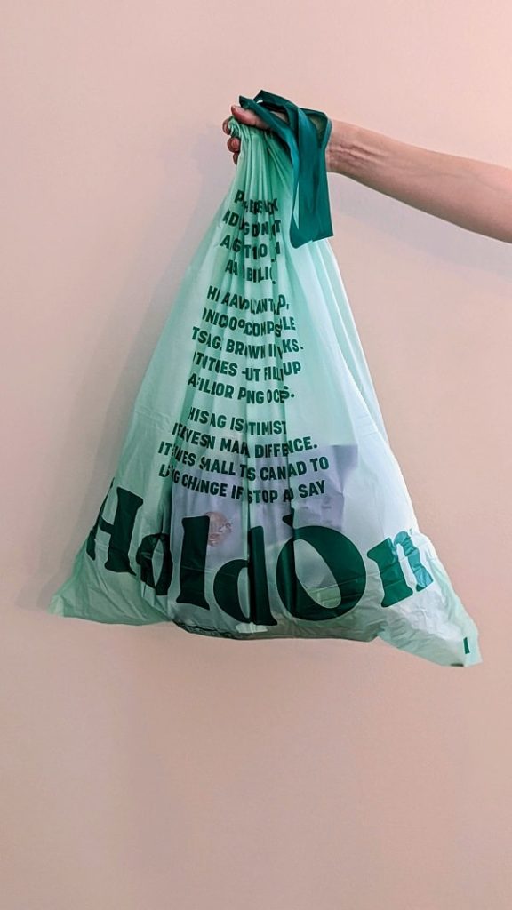 filled holdon compostable garbage bag being held in front of a light pink background
