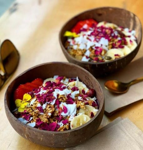 two fruit filled smoothie bowls topped with edible flowers and bananas from kale + coco in dublin