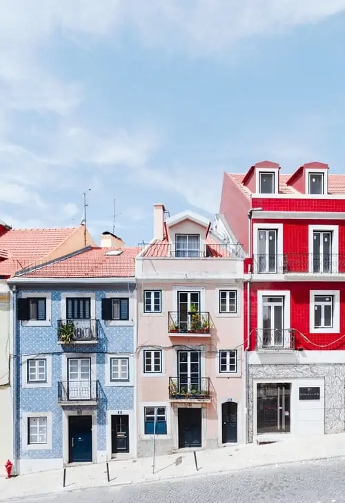 three narrow building on a hill in lisbon one with blue tile work and the other two are pink and red