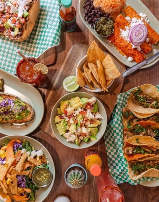 a table filled with authetic vegan mexican dishes like tacos, rice and beans, flautas, and chips at penelope's vegan taqueria in chicago 