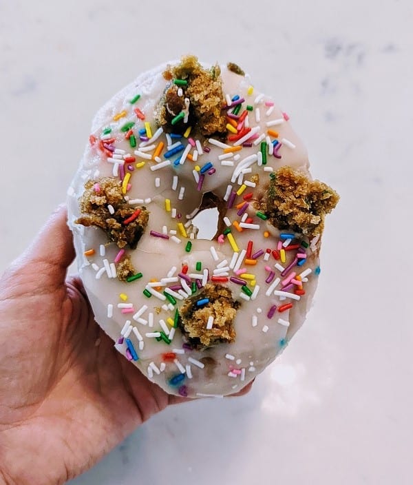 vegan birthday cake donut with white icing, colored sprinkles and chunks of cookie dough from bloomers in toronto