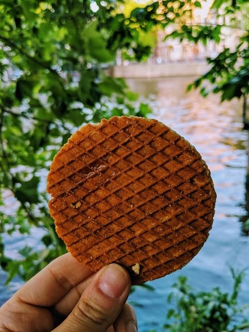 golden brown vegan and gluten free stroopwaffle in front of a canal in amsterdam