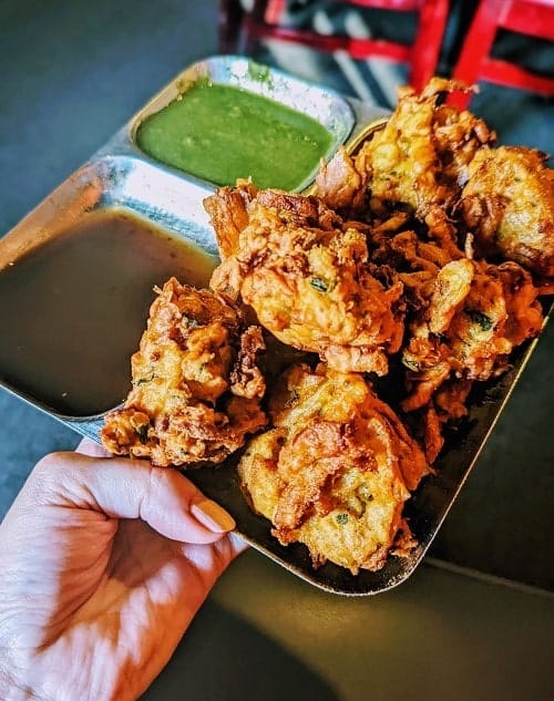vegan gold brown fried veggie pakoras on a silver tray with mint green chutney from woodlands indian restaurant in nashville 