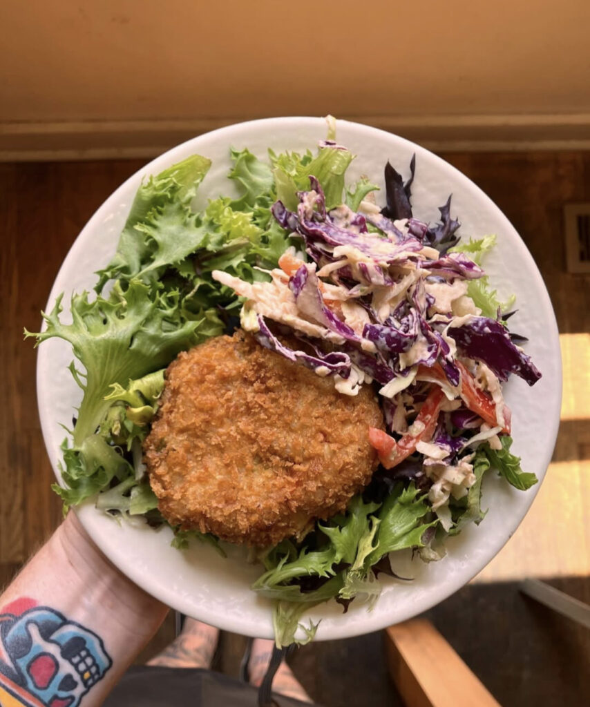 Close-up of a vegan crab cake served over fresh greens with creamy coleslaw on the side at Sunflower Cafe in Nashville.