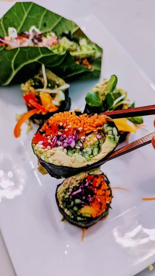 try it raw vegan rainbow roll held with chopsticks over a collard wrap 