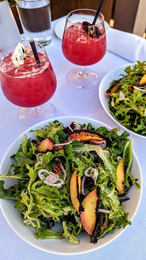 vegan maple peach salads and two pink fruity cocktails on a white tableclothed table at artisan in traverse city