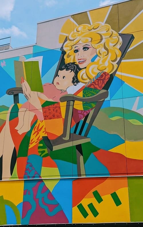 brightly colored mural of dolly parton reading a book to a child in a rocking chair in nashville