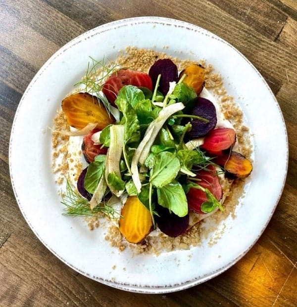 a large white bowl filled with colorful beets and greens on a wood table at fancy radish in dc