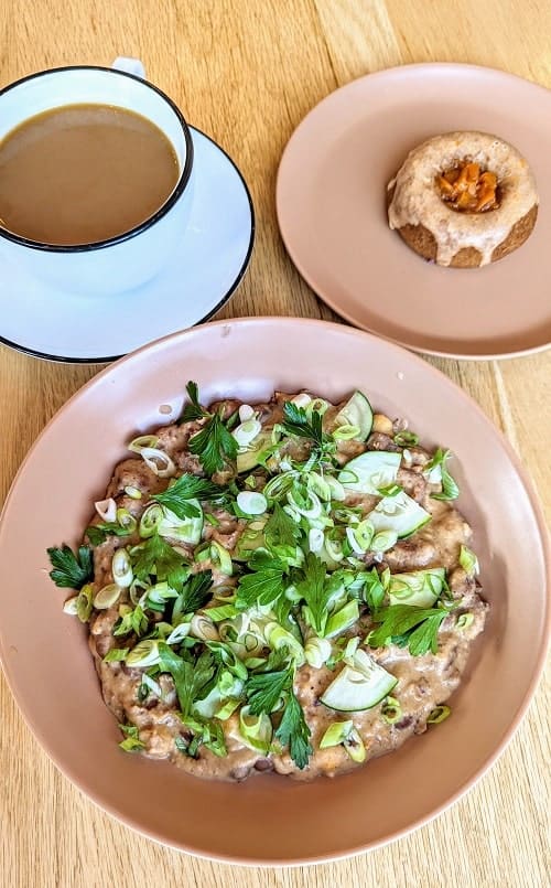 large bowl of foul covered in onions and parsley, vegan donut covered in apricot, and a coffee cup on a sauce at hexenbelle cafe in traverse city