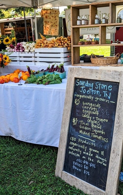 farm stand sign with a table covered in a white table cloth covered in fresh veggies