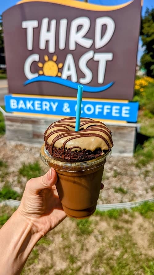vegan mocha choco-latte donut on top of an oatmilk americano in front of the third coast bakery sign in traverse city