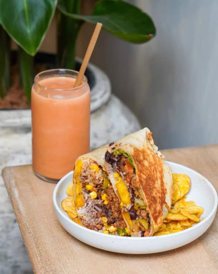 vegan burrito cut into two next to an orange smoothie on a wood table at vegan cuban cuisine in miami