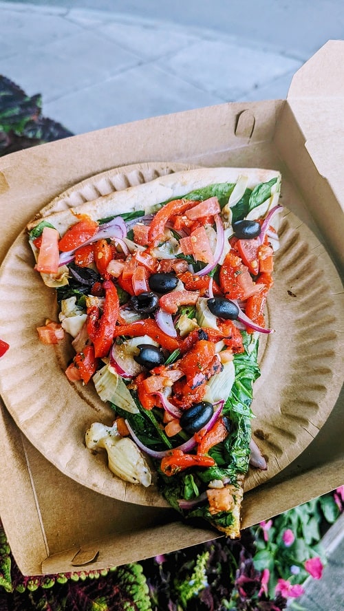 a slice of vegan vegetable pizza in a cardboard box from pizza aroma in ithaca