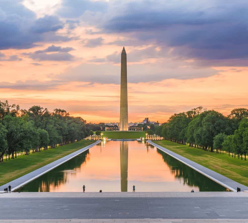 the washington monument in front of the reflecting pool at sunset with a pink and blue sky