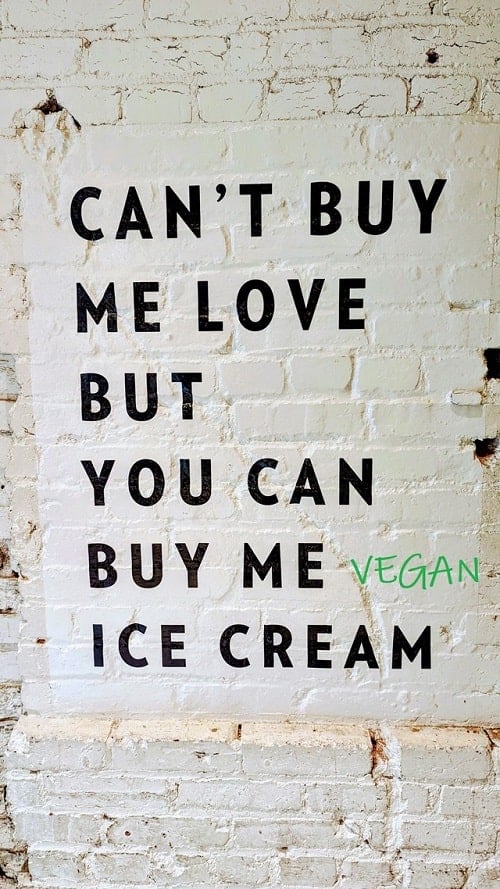 a white brick wall with the message, you cant buy me love but you can buy me vegan ice cream - vegan is added in green