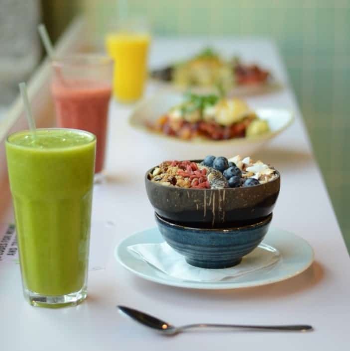 a row of smoothie bowl and colorful smoothies with one blue bowl in the foreground next to a green smoothie on a white table in edinbugh
