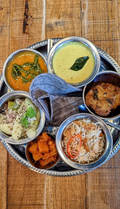 silver platter with five small silver bowls filled with curry, rice, chickpeas, and veggies at marrow in london