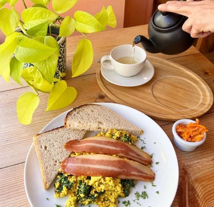 a vegan tofus scramble with two strips of veggie bacon over the top with toast on a wood table next to a green plant at sly fox in edinbugh