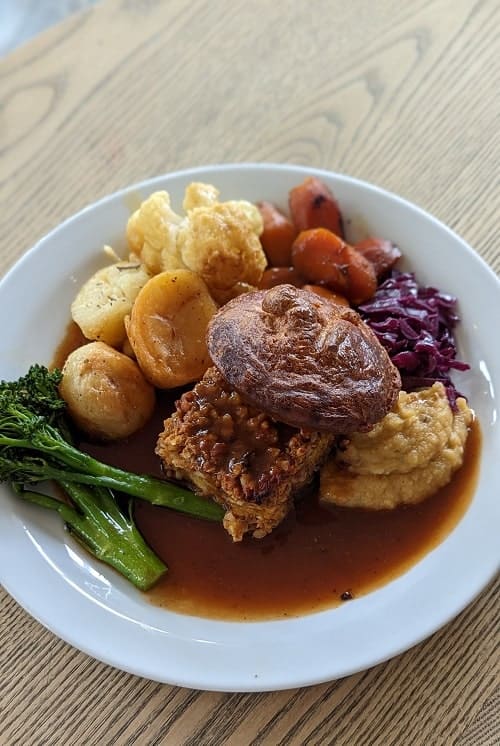 white plate filled with vegan gluten free sunday nut roast, yorkshire pudding, potatoes, broccoli, root mash and gravy at roundhill in brighton