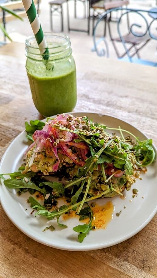 vegan and gluten free avocado toast covered in arugula and pickled onions next to a green smoothie at serenity now in glasgow