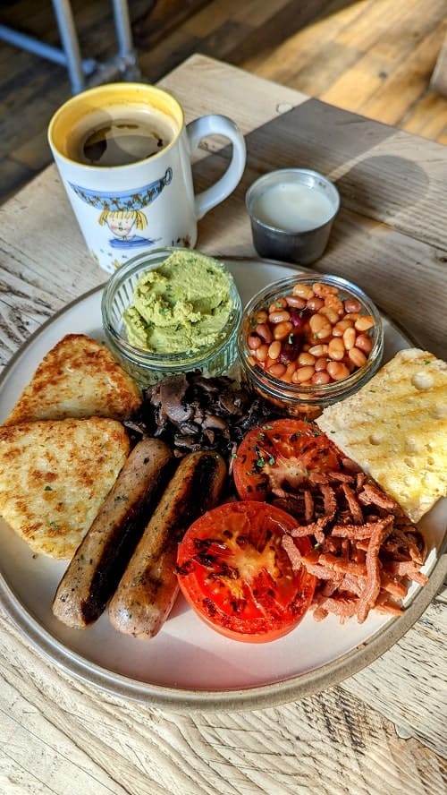 vegan gluten free traditional scottish breakfast with veggie sausage links, grilled tomatoes, mushrooms, toast, pea smash, potatoes, and beans at glasvegan in glasgow