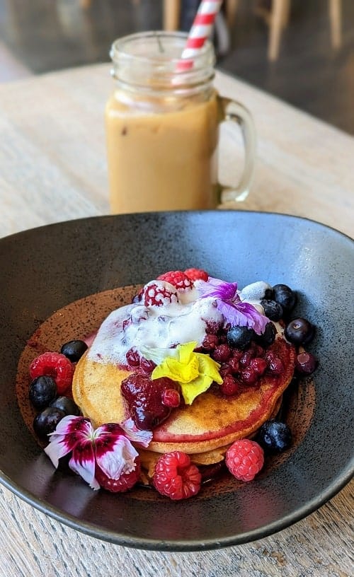 vegan gluten free pancakes in a shallow bowl topped with berries and flower with a glass of iced coffee behind it at wolfox avenue in brighton