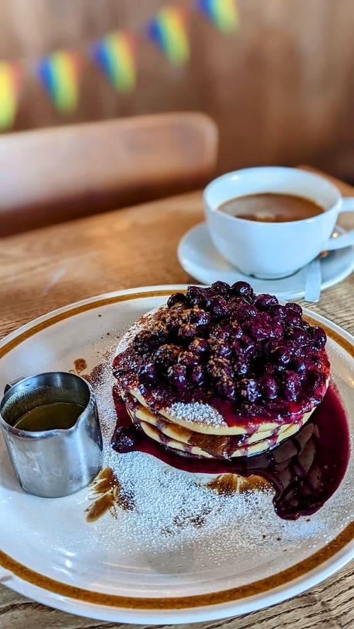 plate of vegan gluten free pancakes topped with blueberry compote with a coffee mug behind it at nowhere man in brighton